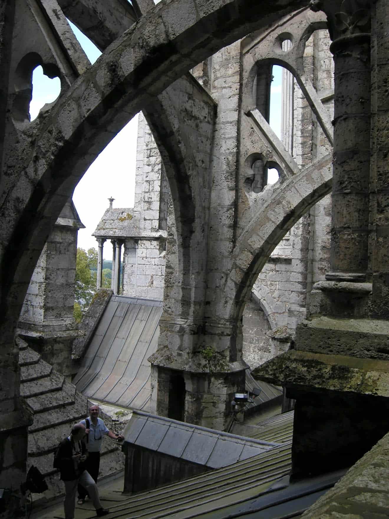 Cathedral roof made of old stone, moss on some areas, two people walking up slanted area, one smiling at camera.